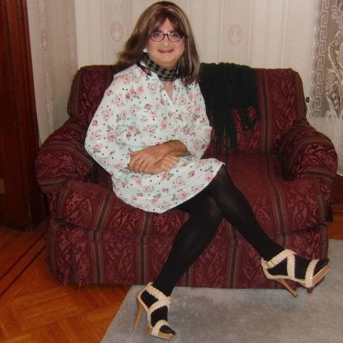 Full-length picture of me, seated, knees left, legs crossed, wearing my new purple cat-eye glasses, 