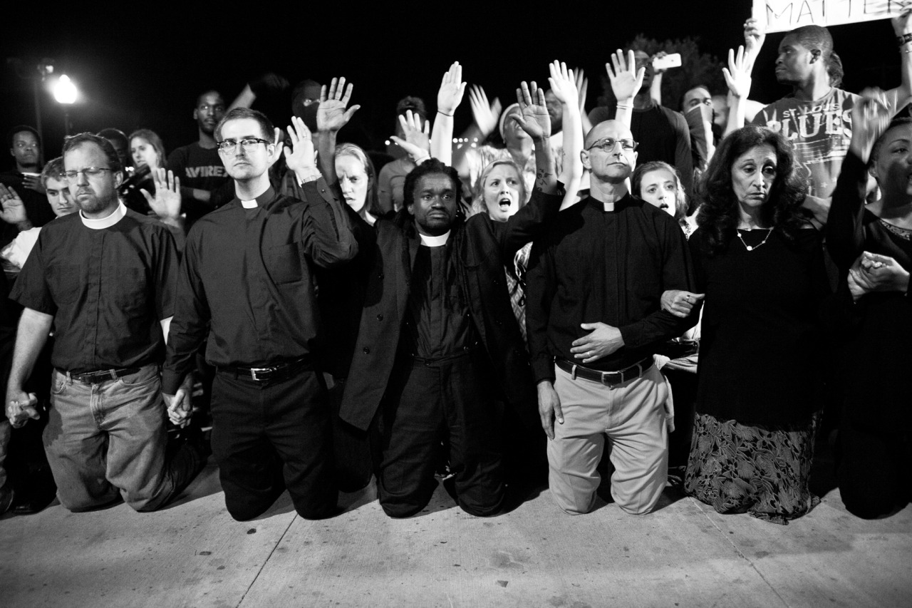 Reverend Osagyefo Uhuru Sekou kneels with fellow clergy members in the driveway of the Ferguson police department in a show of solidarity with protesters on Monday night.
www.AmplifyFerguson.com
Ferguson Police Department ✚ September, 2014