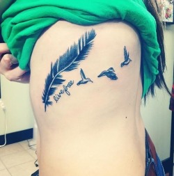 pequenostatuajes:  Pequeño tatuaje de una pluma y tres pájaros volando con la frase “live free” que significa “vive libre”. 