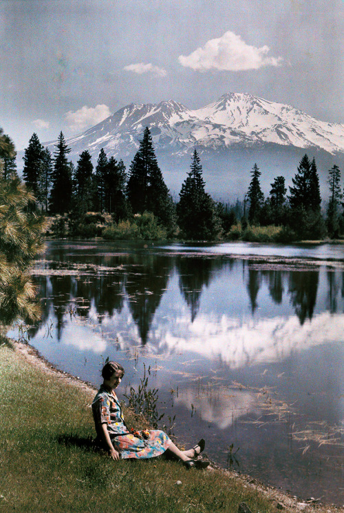 A girl sits by a lake with snow-capped mountains in the background, California, 1929.PHOTOGRAPH BY C