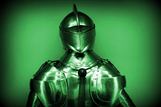 A knight in armor, visor down. The hilt of a sword is visible against the chest. The entire scene is green.