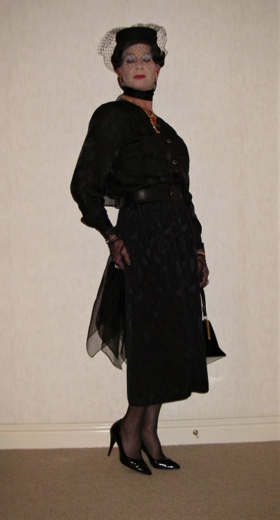 A black satin blouse with satin skirt. Wearing a veiled hat and with chiffon scarves and a handbag