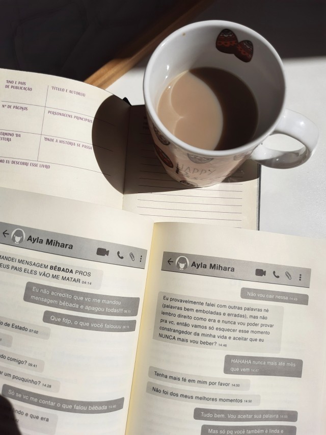 Página aberta de Conectadas da Clara Alves, mostrando um chat de conversas, o livro está em uma mesinha de madeira do lado de uma caneca de café com leite