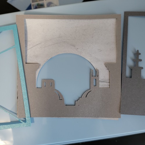 The paper layers are spread out to better show the detail and shapes of the rooftops. A final back layer of white has swirls of black lightly brushed over it and a large circle cut out of the lower part, resembling a sun setting behind the rooftops of the layer above it.