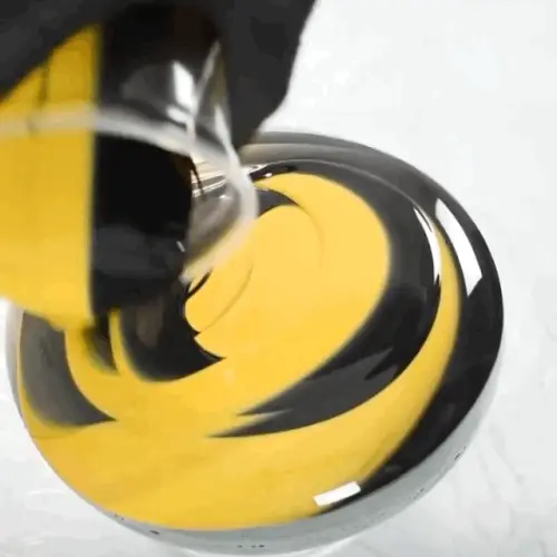 Someone pouring yellow and black paint in a circling motion