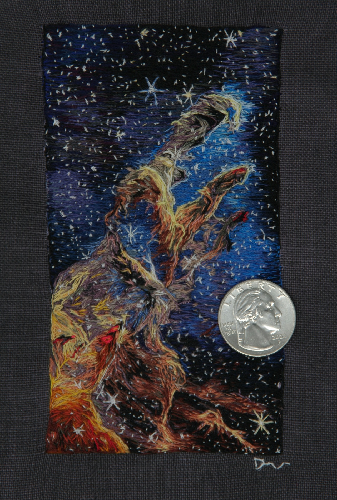 This rectangular piece shows another embroidered interpretation of the Pillars of Creation captured by the Webb Telescope last year. The background is blue and black with white stars scattered from top to bottom. In the middle, three pillars appear in colors of red and yellow. The pillars, which lean to the right, continue downward to the left of the art piece. Credit: Darci Lenker of Darci Lenker Art