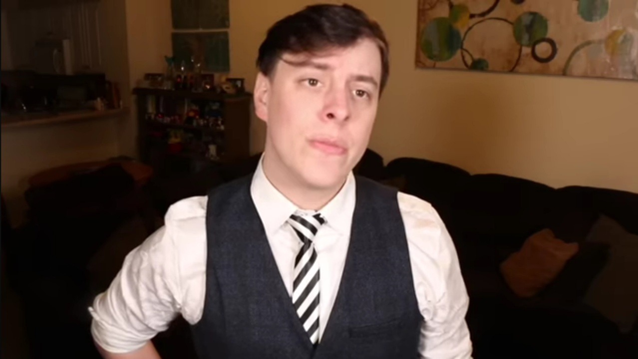 A screenshot of the Sanders Sides video Selfishness vs Selflessness Redux, showing Thomas Sanders standing in his living room, wearing a white shirt, black waistcoat, and black-and-white striped tie.