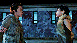 A gif from the performance music video. Ten is wearing a brown fur outfit while Hendery is wearing a light grey outfit. Instead of leaning in close like they usually do on stages, they mimic fighting in this version.