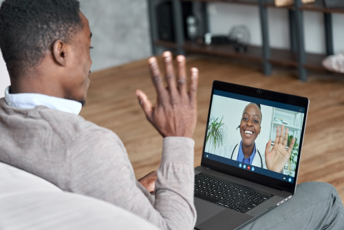 A male patient talking on a conference video call to a female doctor. Adobe stock photo.