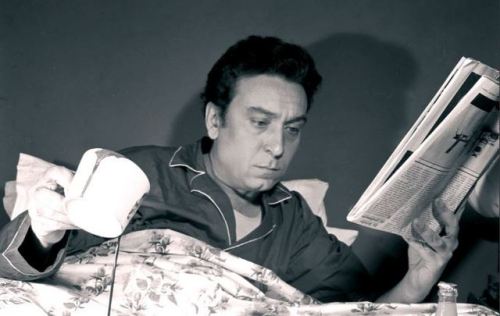 Luciano Bianciardi in posa nel suo letto mentre rovescia la cioccolata calda.