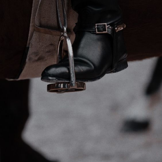 An image of a black riding boot in a stirrup on a saddle from the foot down.