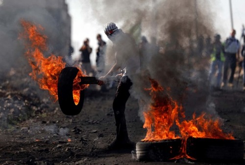  A masked protester holds a burning tyre during clashes with Israeli troops in the village of Kofr Q