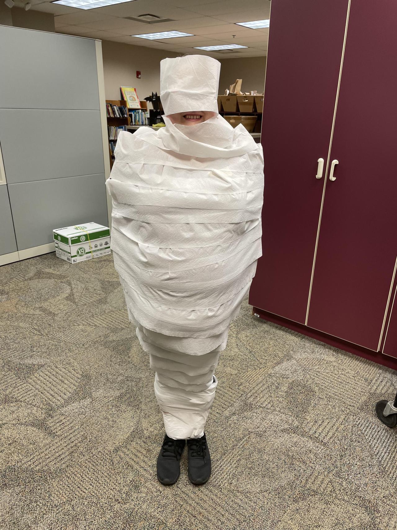 The librarian is completely wrapped head to toe in toilet paper. You can still see her grin
