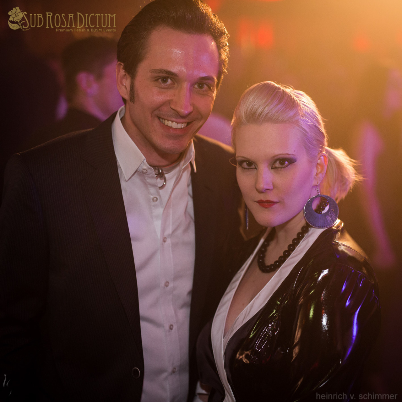 Eine blonde Latex-Herrin präsentiert ihren mit einem Metallhalsreif gekennzeichneten