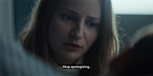 Text reads: Stop apologizing. A white woman with brown eyes and dark blonde hair speaks wearing cream knit turtleneck. She is lit by white light from the window behind her.