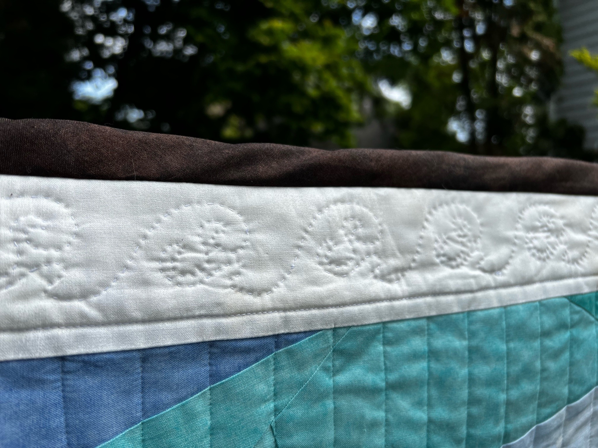 detail of the above quilt border, white stitching on white fabric in a wave pattern 