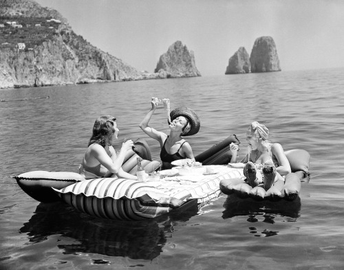 hauntedbystorytelling:Three young women eat spaghetti on inflatable mattresses at Lake of Capri, 193