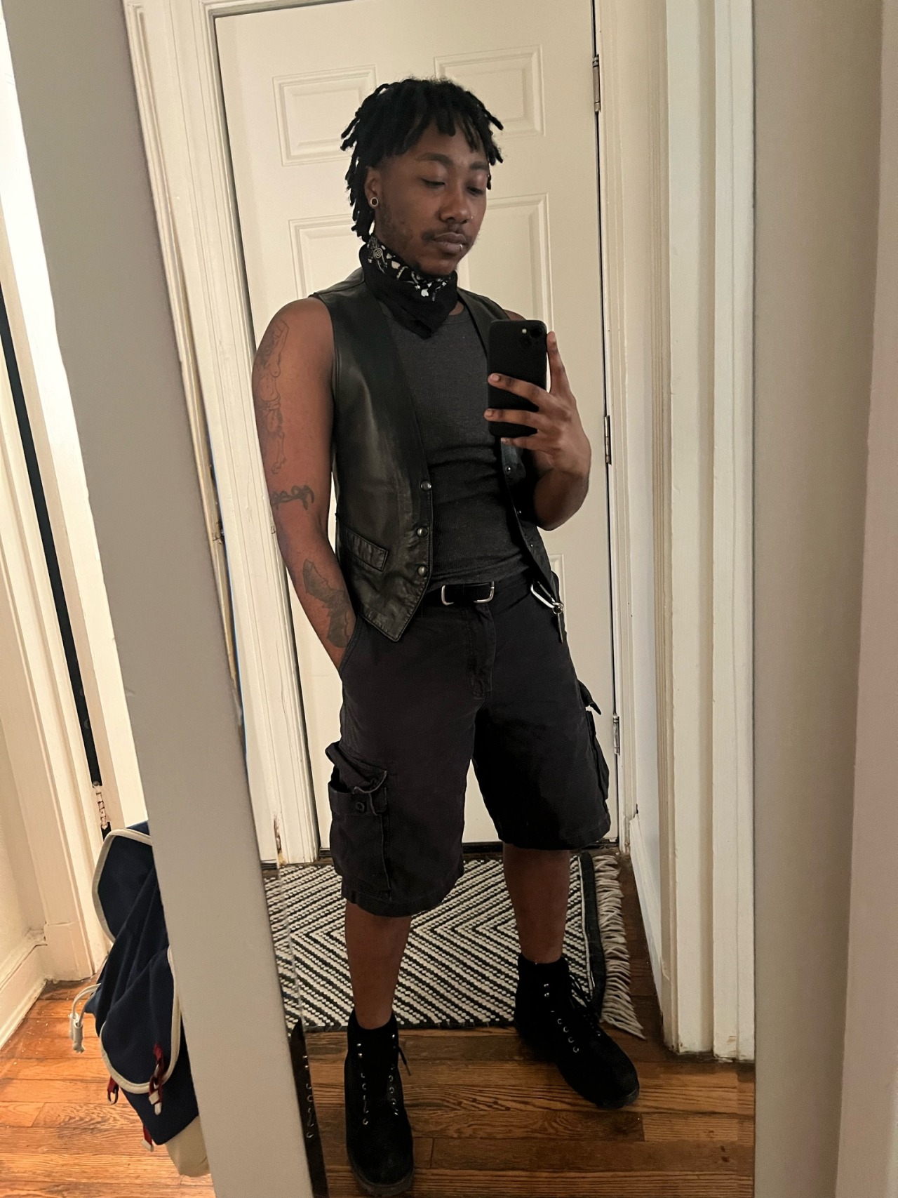 all black: a leather vest over tank top and cargo shorts. a bandana tied around the neck and work boots.