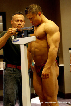 muscletits:  Like a prized steer led to auction, the bodybuilder stands and lets the clothed men determine their worth. 