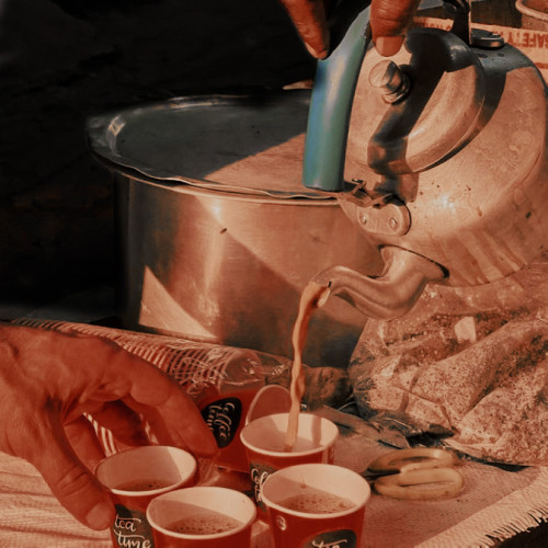brown hands serving tea from a copper kettle into paper cups. 