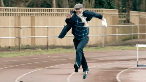 [ID: Five Screencaps Of Dave Gorman On Taskmaster, Traversing An Outdoor Athletics Track With Comically