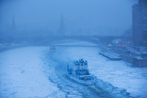 Two ice breakers move along the frozen Moskva River with the Kremlin in the background during snowfa