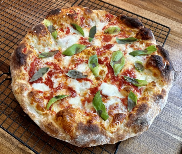 Photo of a puffy, blistered 14" cheese pizza with basil