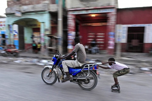 A child on rollerblades hitches a ride from a motorbike in Port-au-Prince, Haiti on October 25, 2015