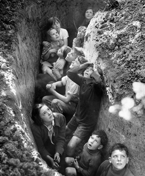 historicaltimes: Children take refuge in a trench whilst watching a dogfight unfold in the skies abo