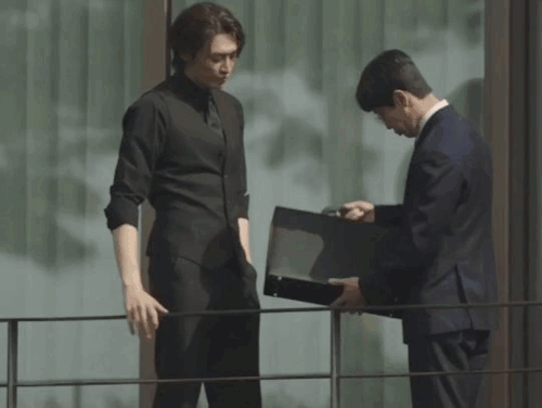 doyoung leaning onto a metallic support while attorney han looks into a suitcase, before looking up at him