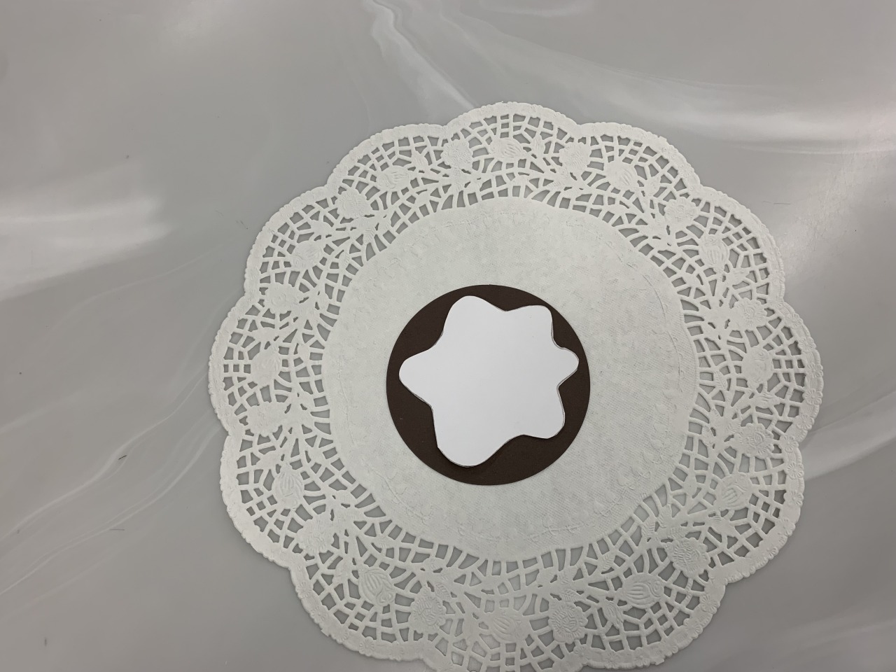 An in progress cookie, showing a brown paper circle and a white paper blob on a doily