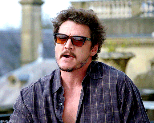 dieter bravo in sunglasses and an unbuttoned blue shirt, not really smiling, playing with his tongue in his mouth, looking mischievous i guess? idk he's so cool