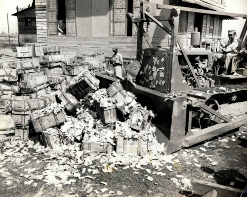 An American GI uses a bulldozer to plow Japanese “Mickey Mouse” money into large piles, 