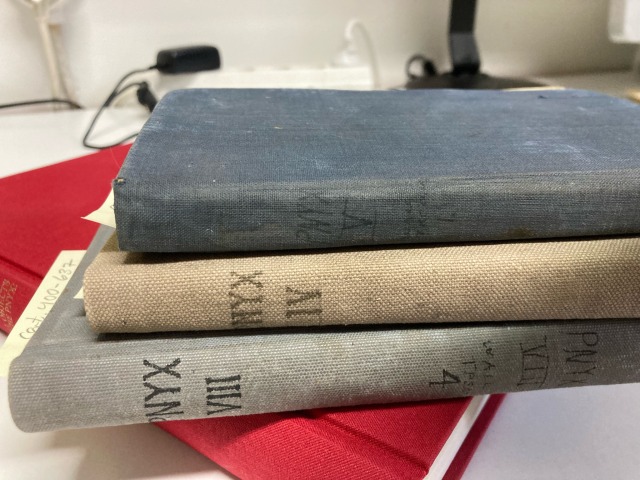 a stack of three blueish gray notebooks on top of a red book