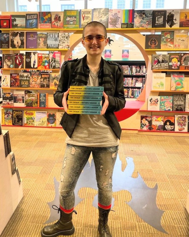 Finn Longman holding a stack of copies of The Butterfly Assassin in Waterstones Piccadilly