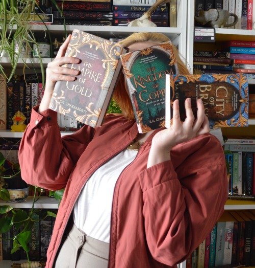 me, in front of my bookshelves, holding three books in front of my face