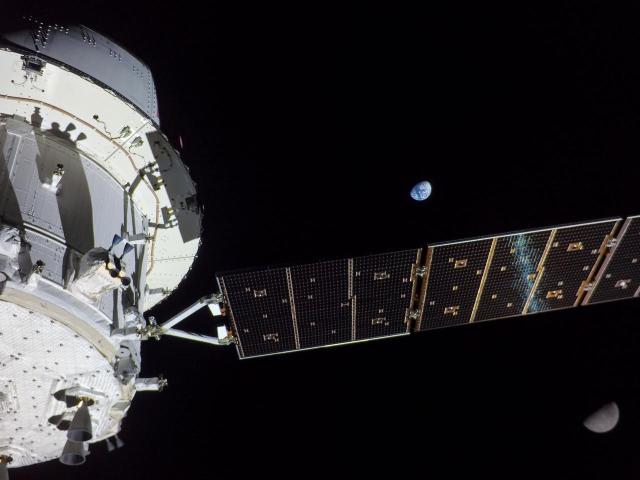 On flight day 13 of the Artemis I mission, Orion captured this view of Earth and the Moon on either sides of one of the spacecraft’s four solar arrays. The spacecraft is white and gray and stands out against the blackness of space. Credit: NASA