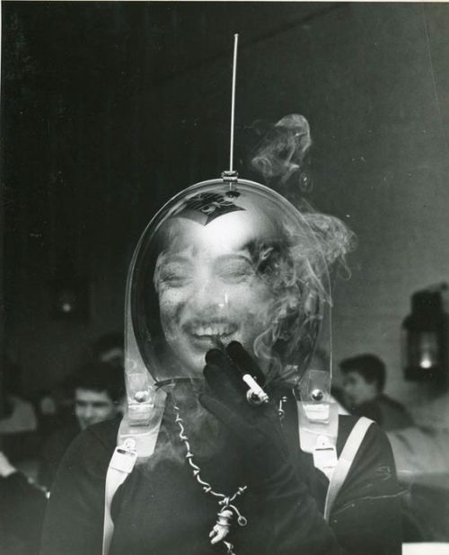 Weegee, Woman in a Space Helment Smoking a Cigarette ca. 1950