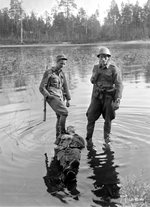 bag-of-dirt:Finnish soldiers stand in lake Paanajärvi over the dead body of an enemy Sovie