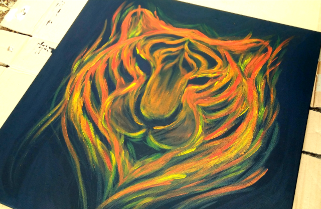 1 of 3 images from various angels showing a large square canvas painting depicting the face of a tiger painted with streaks of res, orange, and yellow flames against a black backdrop. The painting is signed by myself as Natch.