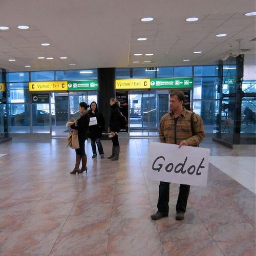 dapurinthos:[a man stands in the arrivals section of an airport, holding a sign that reads “godot”.]