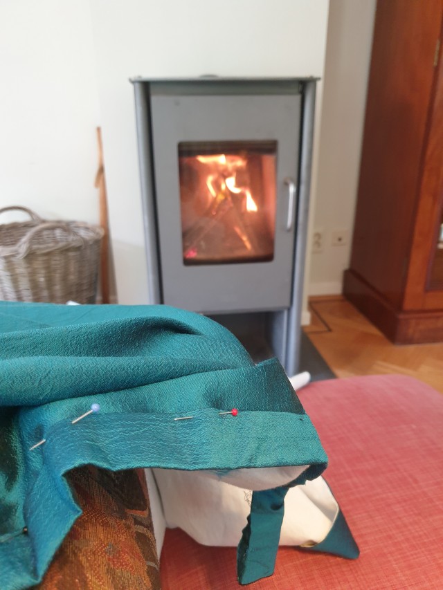 a photo of a seagreen silk skirt with the waistband still pinned, in the background is a lit stove with merry flames 