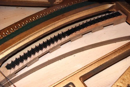 <p>In fact, all four of the middle ‘feet’ were detached. This was the source of the burbling rattle, when the sustain pedal was on and all the bas strings vibrating. Their combined motion was causing the bridge feet to vibrate against the shelf to which it should have been securely attached.</p>