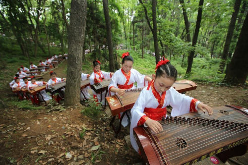 Teenagers dressed up in traditional costumes play the Chinese instrument Zheng in the Gulongzhong sc