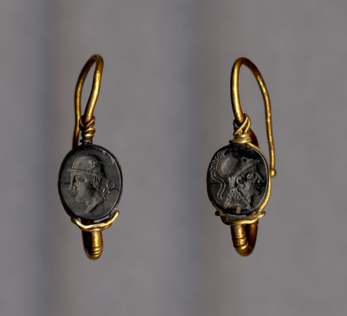 records-of-fortune:One of a pair of gold earrings, set with a black glass seal engraved with a head 