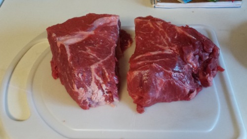 A chuck roast, resting on a plastic cutting board. It is cut in half.