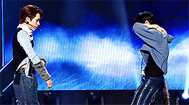 A gif from their performance at MusicCore. Ten is wearing a blue cropped hoodie and Hendery is wearing a black and blue patterned shirt with grey fur sleeves.