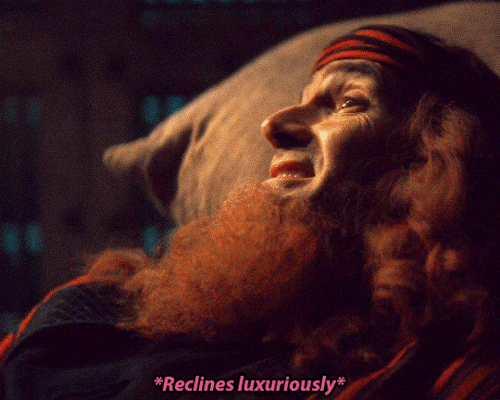 Gif of a scene from the Good Omens season 2 episode 2 minisode where Crowley reclines on stacked sacks in the basement of Job's house. The subtitles say: *Reclines luxuriously*