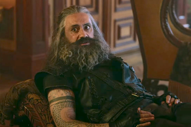 An image of Taika Waititi as Edward Teach in Our Flag Means Death. He's sitting on a divan in the captain's cabin on the Revenge and he looks a little startled or concerned.