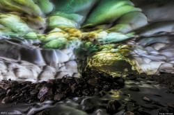 sixpenceee:  Cave at the Mutnovsky Volcano, RussiaThis ice cave formed at the base of a volcano. Hot springs have carved out the cave’s incredible shapes, while light that filters in through the roof creates an incredible color display of greens, purples,